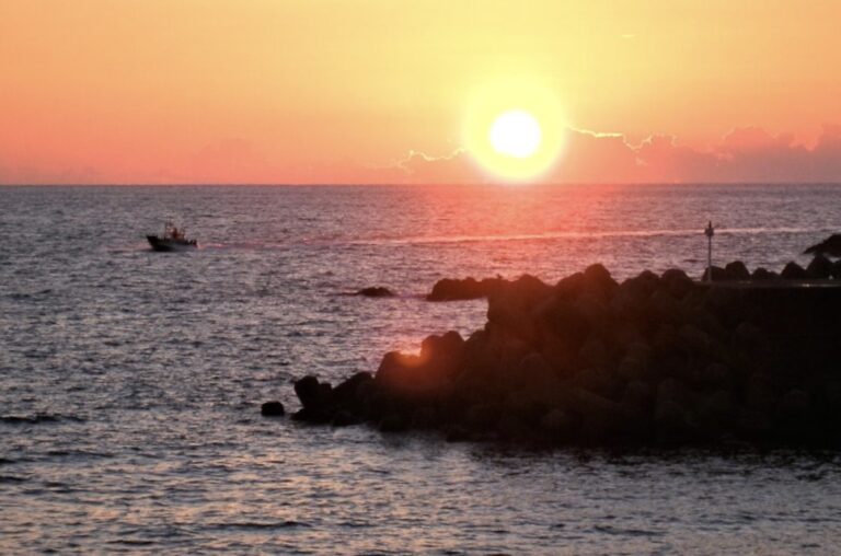 日本海に沈む夕日の輝きの中、漁船が加茂港に帰ってくる
